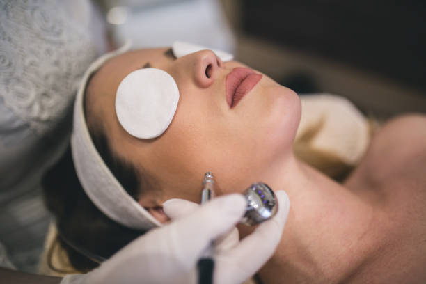 Close-up top-view side-view portrait of a young woman with a towel on her head lying on a table with closed eyes getting a laser skin treatment in healthy beauty spa salon