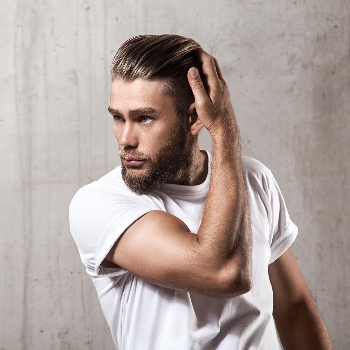 Handsome bearded man in a blank white t-shirt with stylish hair on a cement wall